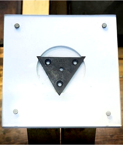 Triangular piece of metal with drill holes mounted on a white board